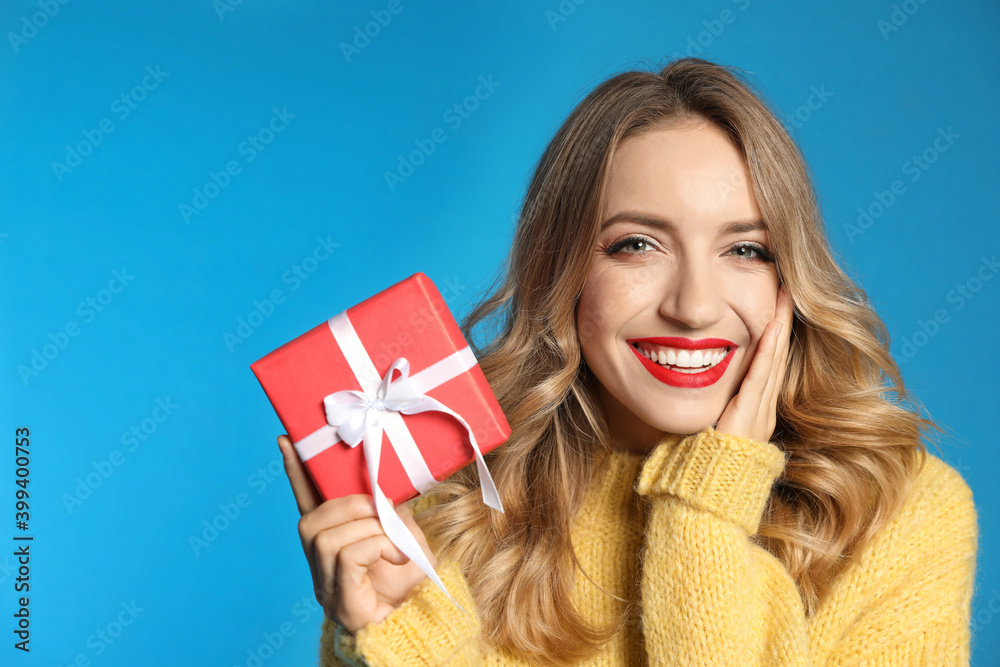 Happy young woman with Christmas gift on light blue background Happy young woman with Christmas gift on light blue background