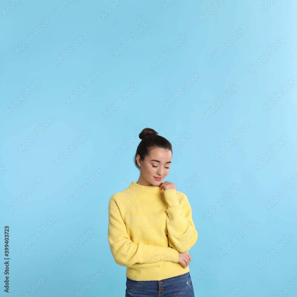 Beautiful young woman wearing yellow warm sweater on light blue background. Space for text