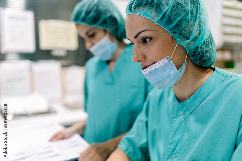 Female doctors in uniforms and masks using computer at table Female doctors in uniforms and masks using computer at table