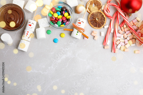 Flat lay composition with funny snowmen made of marshmallows on light marble table, space for text. Bokeh effect