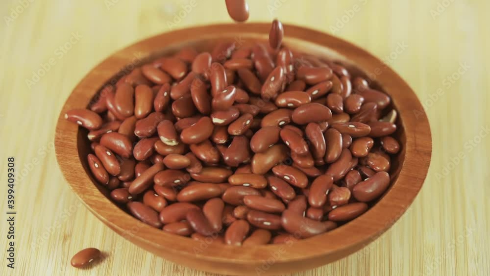 Red kidney beans falling into a wooden bowl that's on a bamboo table Red kidney beans falling into a wooden bowl that's on a bamboo table