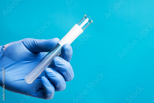 medical person or scientist holding glass test tube isolated over blue background. blank white label. copy space