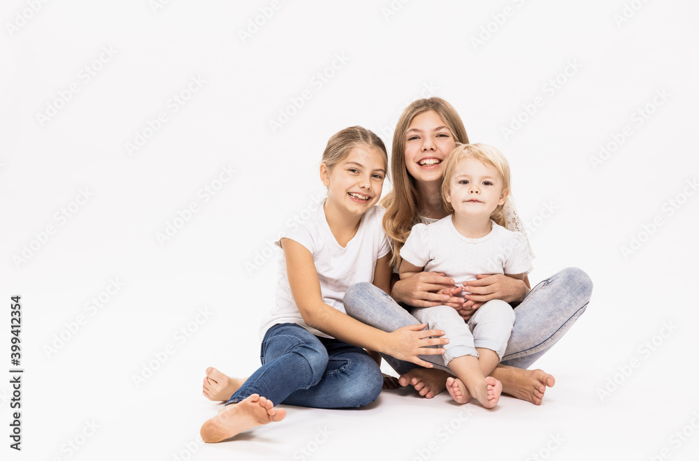 Female toddler sitting on elder sister's lap against white background in studio Female toddler sitting on elder sister's lap against white background in studio