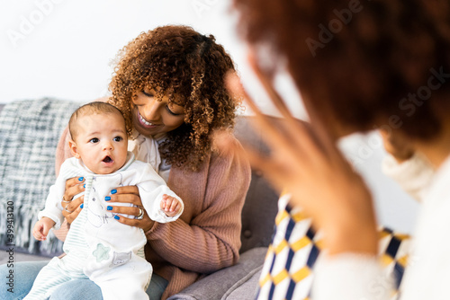 Female toddler looking at aunt doing hand gesture sitting on sofa in living room