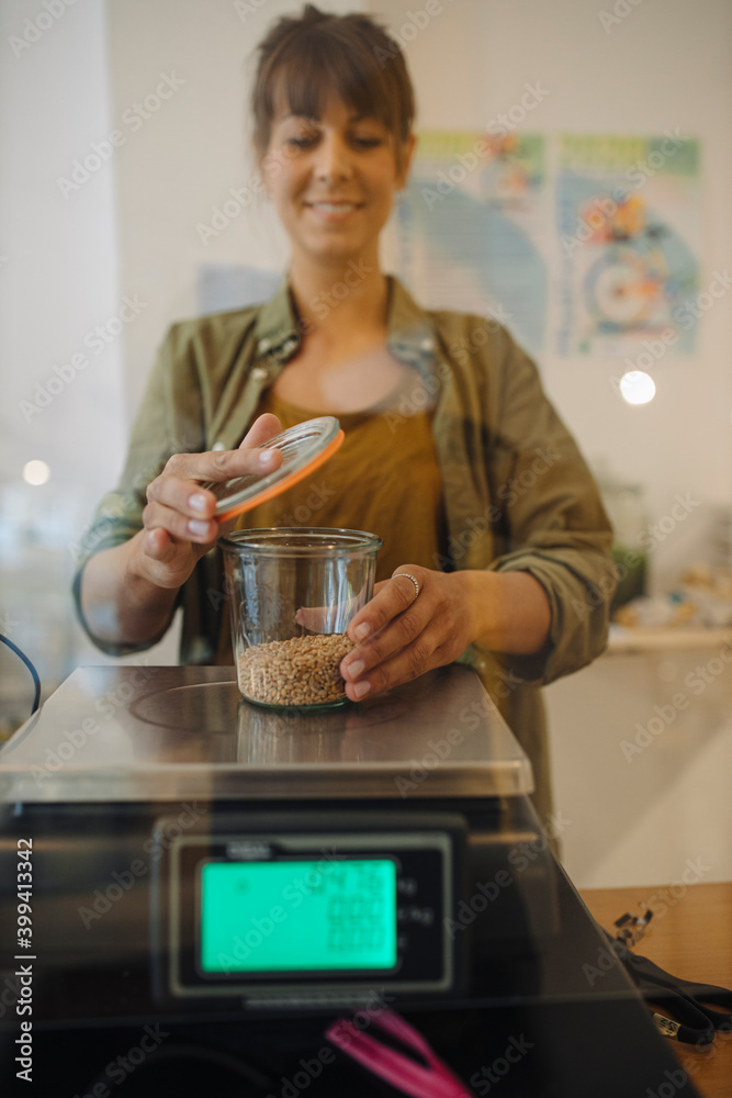 Female owner weighing grain jar on weight scale in cafe Female owner weighing grain jar on weight scale in cafe