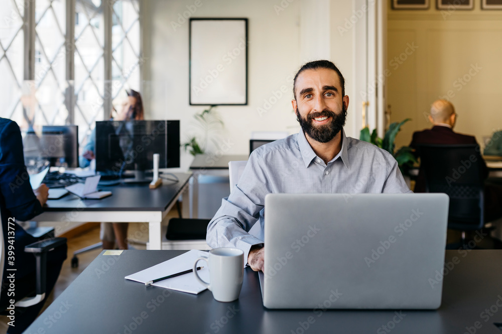 Confident hipster entrepreneur working on laptop at desk in office Confident hipster entrepreneur working on laptop at desk in office