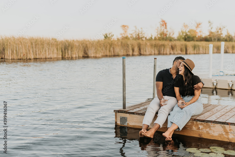Man with wineglass kissing woman while sitting on pier Man with wineglass kissing woman while sitting on pier