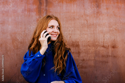 Smiling young woman talking on smart phone against wall photo