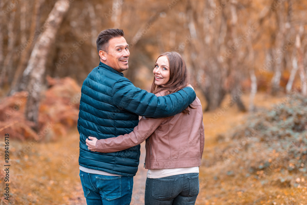 Smiling couple looking over shoulder while standing in park during autumn Smiling couple looking over shoulder while standing in park during autumn