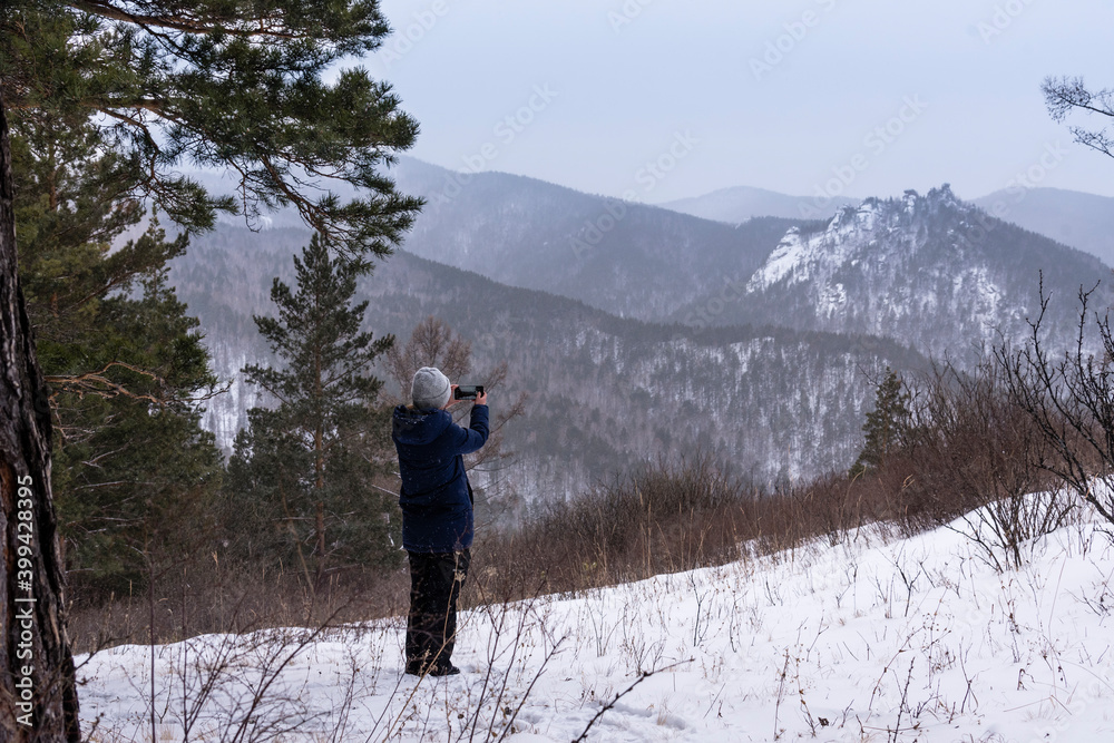 A young girl makes a photo on a mobile phone of a rocky ridge in winter. Beautiful landscape, hike, outdoor activities, tourism.