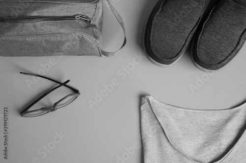 Top view of a gray men's fashion t-shirt, glasses, toiletry bag  and a pair of sneakers in a gray background