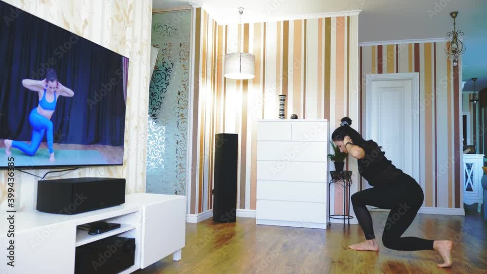 Online workout, remotely. Young woman, in sportswear, watching tutorial video with fitness coach on TV and practicing exercises at home. doing sports during lockdown, at home