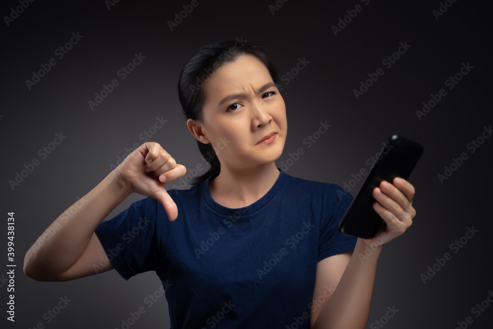 Asian woman looking at smart phone and showing thumb down. Asian woman looking at smart phone and showing thumb down.