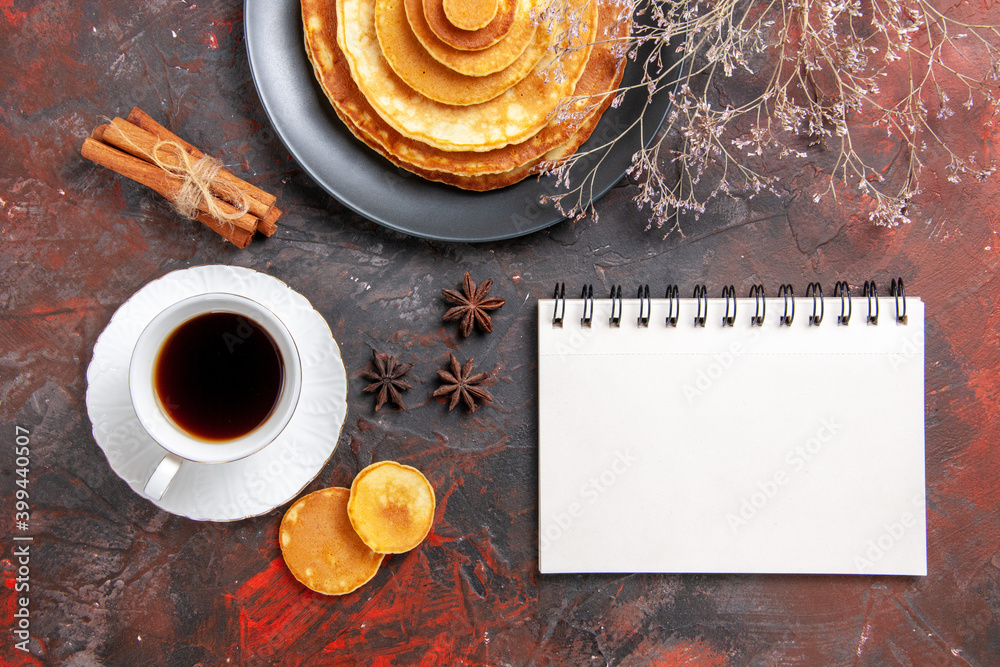 Breakfast with pluffy pancakes and tea in awhite cup next to notebook Breakfast with pluffy pancakes and tea in awhite cup next to notebook
