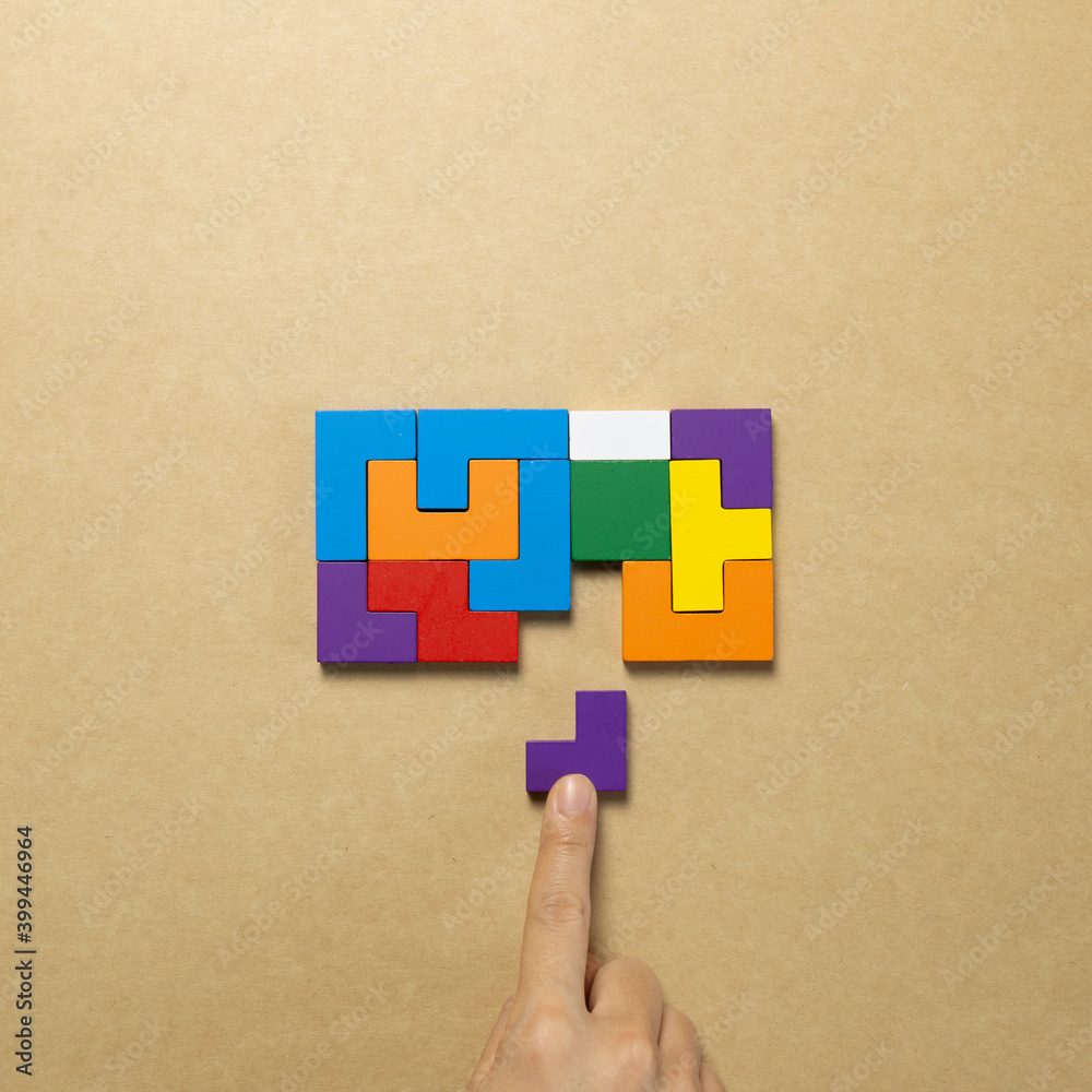 Set of color blocks puzzle pieces and hand holding last one piece on brown background. Creative thinking, idea, problem solving, success concept. top view