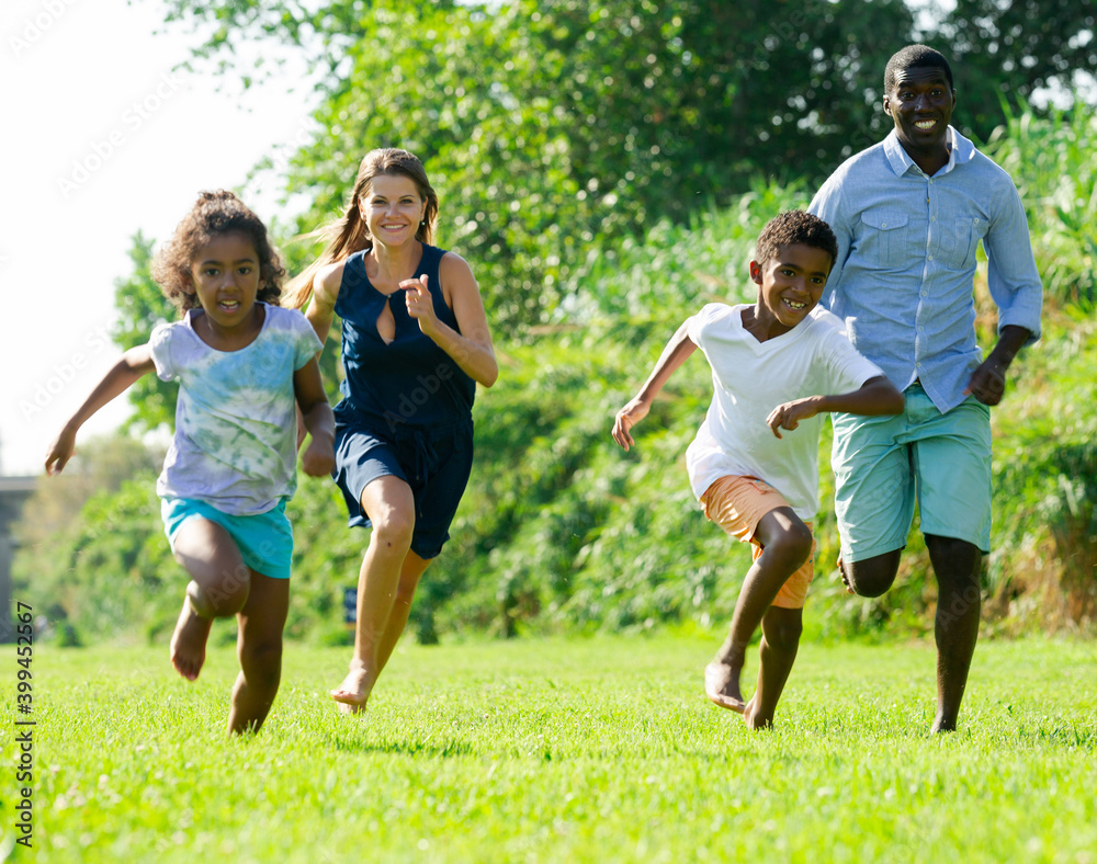 Happy preteen children with parents enjoying time together, running on green lawn in park