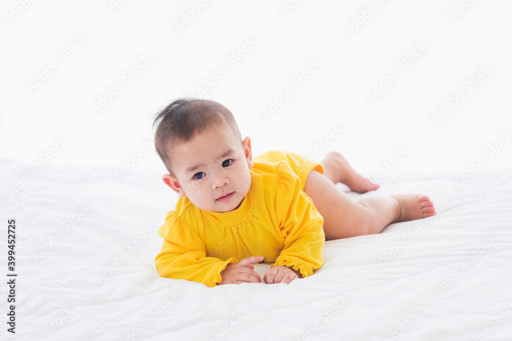 Portrait of beautiful young Asian newborn little baby prone on the bed at home, Happy baby smile wears a yellow shirt relaxing in the room, Family morning at home Portrait of beautiful young Asian newborn little baby prone on the bed at home, Happy baby smile wears a yellow shirt relaxing in the room, Family morning at home