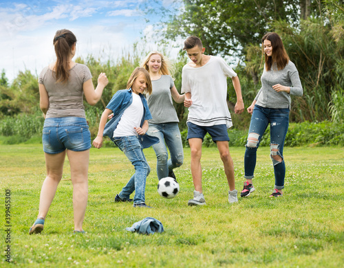 Group of teenagers having fun and kicking football in park on summer day