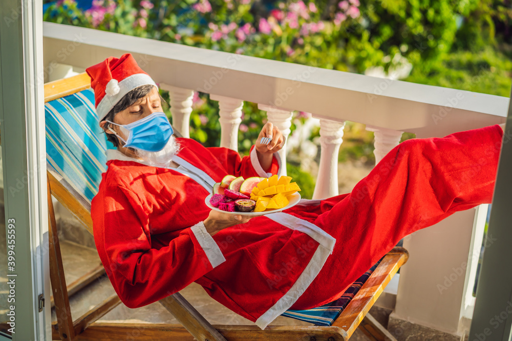 Obraz premium cheerful santa man in a medical mask hold exotic fruit. healthy gift. christmas during coronavirus COVID 19. bearded man healthy eating. merry christmas. happy new year. xmas gifts and presents