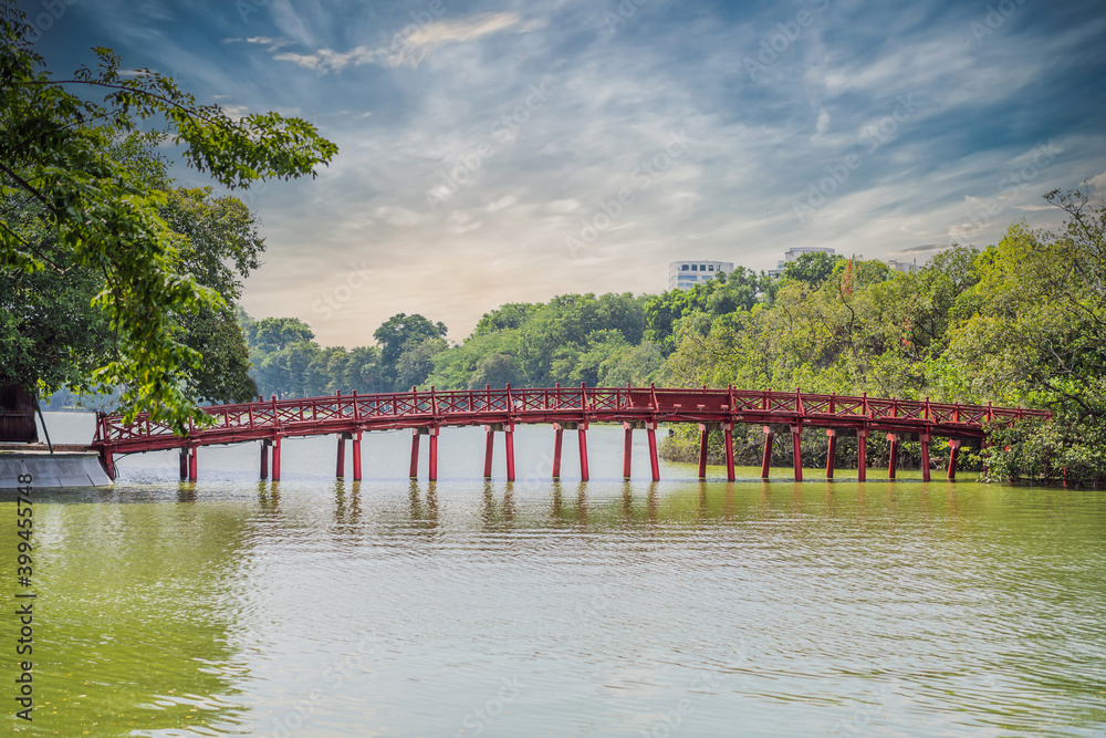 The Red Bridge in public park garden with trees and reflection in the middle of Hoan Kiem Lake in Downtown Hanoi. Urban city at sunset, Vietnam. Cityscape background