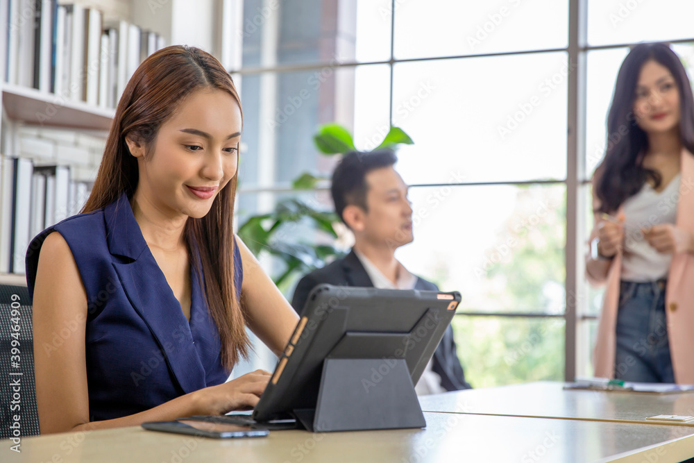 Business woman using modern digital tablet while coworker interacting in the background in the office , Teamwork meeting and partnership concept. Business woman using modern digital tablet while coworker interacting in the background in the office , Teamwork meeting and partnership concept.
