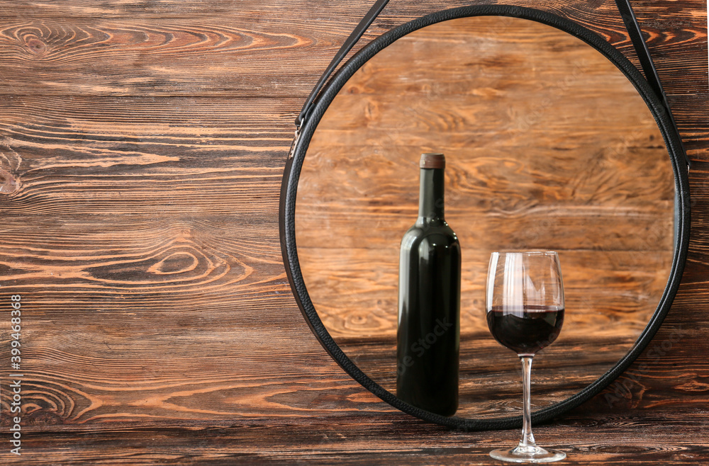 Glass of wine looking at its reflection in mirror on wooden background