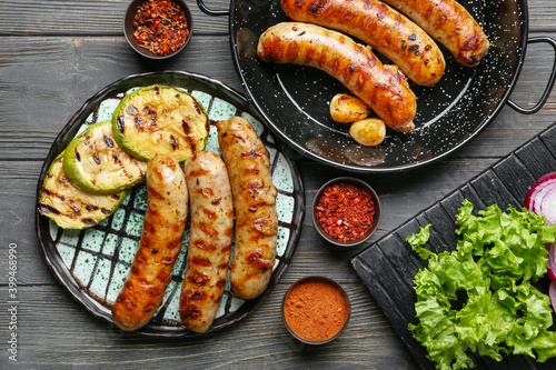 Plate with delicious grilled sausages, vegetables and spices on table