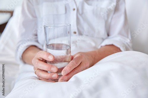 medicine, healthcare and people concept - close up of senior woman with glass of water sitting in bed at hospital ward