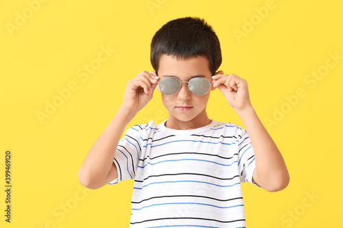 Cute boy wearing stylish sunglasses against color background