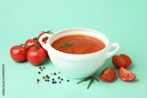 Bowl with tomato soup and ingredients on mint background