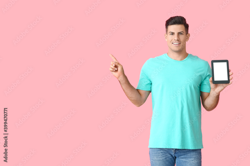 Young man with e-reader pointing at something on color background