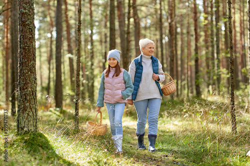 picking season, leisure and people concept - grandmother and granddaughter with baskets and mushrooms walking in forest