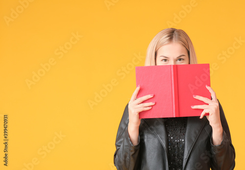 Beautiful young woman reading book on color background