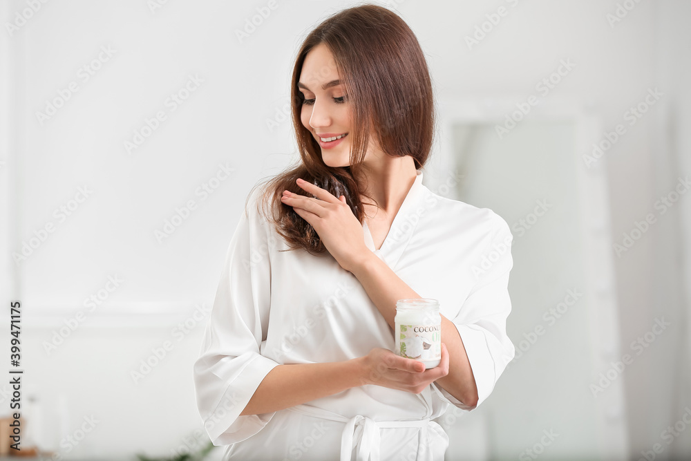Beautiful young woman applying coconut oil on hair in bathroom Beautiful young woman applying coconut oil on hair in bathroom