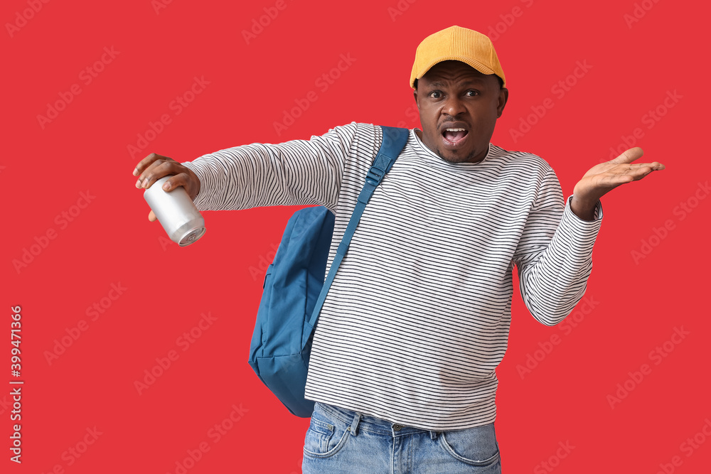Displeased African-American man with empty soda can on color background