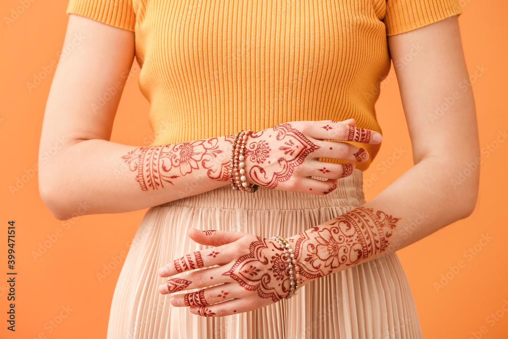 Beautiful woman with henna tattoo on hands against color background