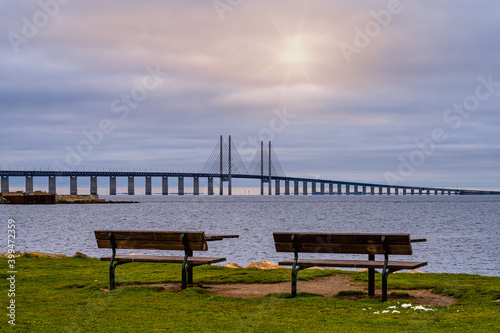 Two benches in front of a beautiful ocean view with a bridge. Blue ocean and a sunset sky in the background. Picture from Malmo, southern Sweden © Dan