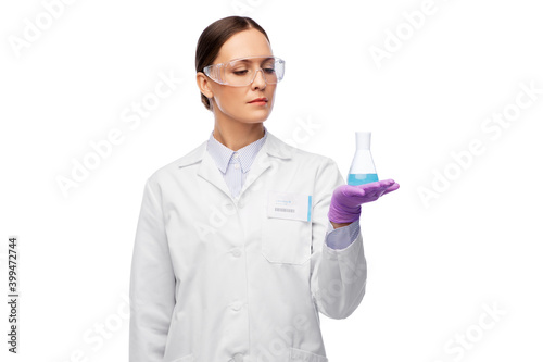 science  chemistry and people concept - young female scientist in goggles with chemical in flask making test or research