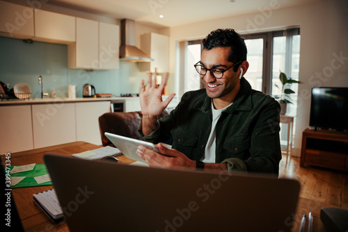 Mixed race businessman waving to digital tablet while interacting on video call with clients