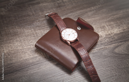 Brown wristwatch and wallet on the wooden background.