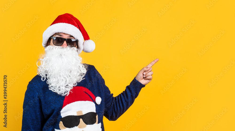 happy male hipster with beard and moustache wearing santa hat for xmas party celebration pointing finger on copy space, winter holidays
