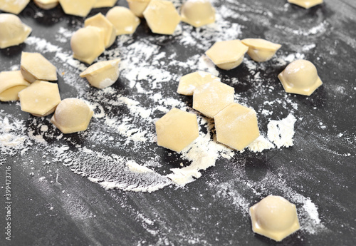 Dumplings, ravioli close-up, hexagonal shape of dough on a black table. Dusted with flour and spread by hand.