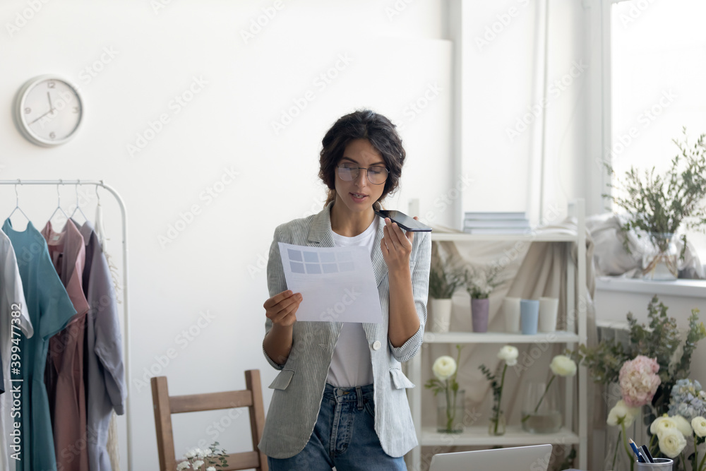 Using audio app in work routine. Smart young lady florist search information online using virtual digital assistant. Female designer dictate voice message to supplier ordering chosen fabric pattern Using audio app in work routine. Smart young lady florist search information online using virtual digital assistant. Female designer dictate voice message to supplier ordering chosen fabric pattern