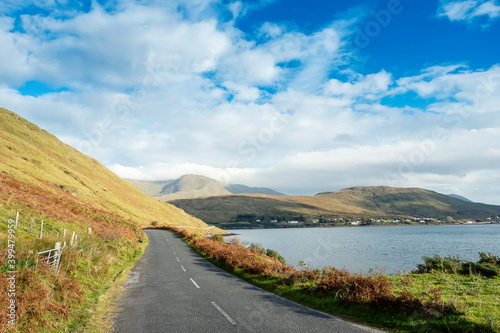 Small asphalt road with beautiful scenery, Killary fjord, Connemara, West of Ireland. Travel and transportation concept. Warm sunny day, Cloudy sky. Nobody