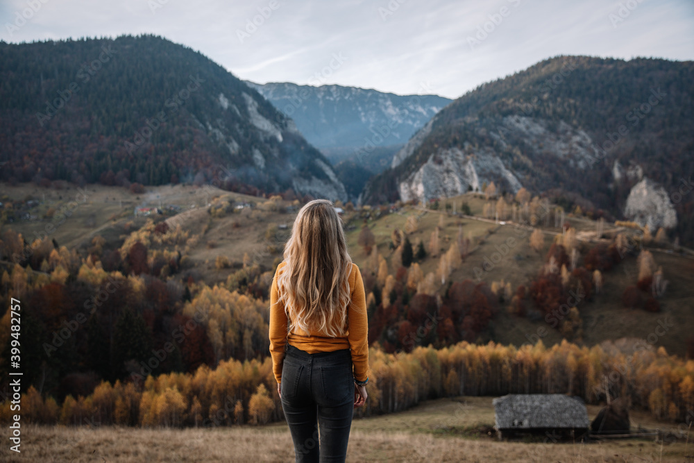Rear view of young blonde female standing and enjoying the autumn mountains. Travel and lifestyle concept. Transylvania,Romania,Europe.