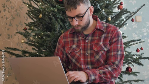 Busy freelnacer man working on laptop under christmas tree. Christmas online shopping. male buy order on laptop computer xmas presents gifts. typing and searching internet, looking for xmas sales  photo