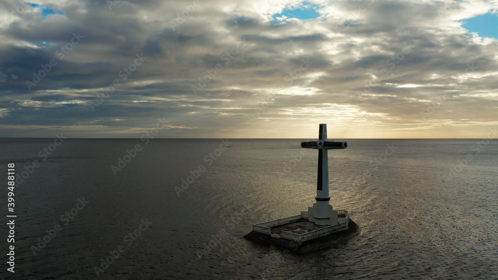 Catholic cross in sunken cemetery in the sea at sunset, aerial drone. Large crucafix marking the underwater sunken cemetary, Camiguin Island Philippines.