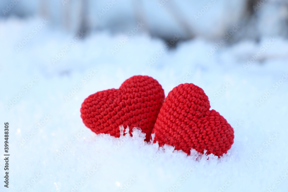 Fototapeta premium Valentine's hearts on a snow in winter forest. Two red knitted symbols of love, background for romantic greeting card