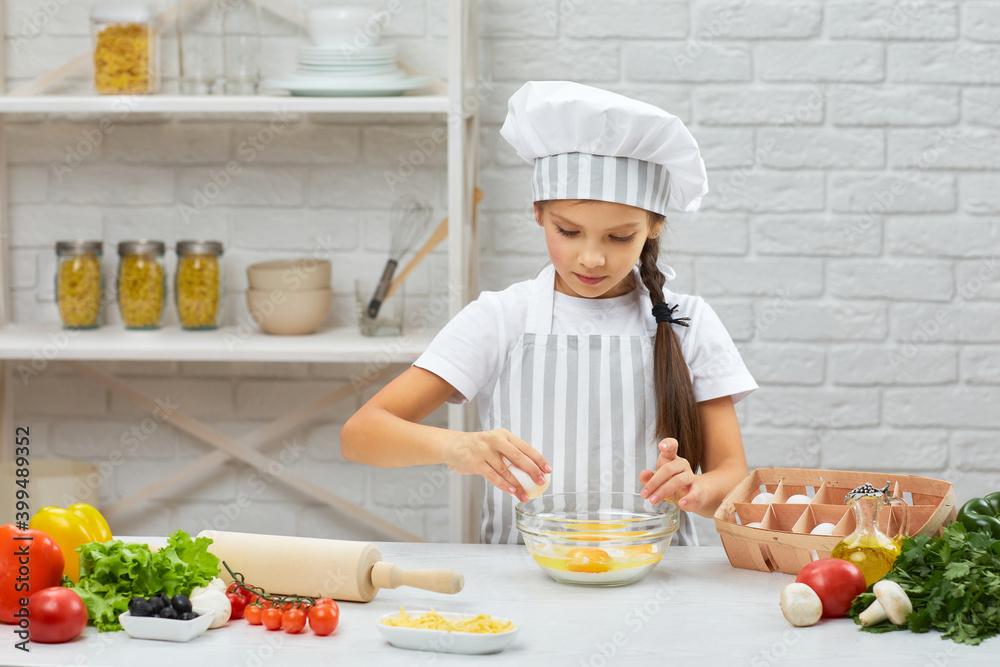 cute little girl in chef hat and an apron is breaking yellow egg into fresh dough in the kitchen. child cooking with dough cute little girl in chef hat and an apron is breaking yellow egg into fresh dough in the kitchen. child cooking with dough