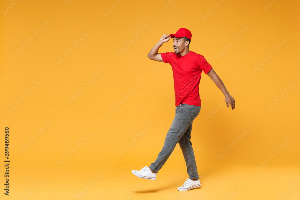 Full length delivery employee african man 20s in red cap blank print t-shirt uniform workwear work courier dealer service during quarantine covid-19 virus concept isolated on yellow background studio. Full length delivery employee african man 20s in red cap blank print t-shirt uniform workwear work courier dealer service during quarantine covid-19 virus concept isolated on yellow background studio.